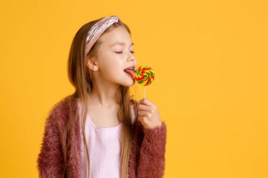 Küçük kız okul tatilinde lolipoplardan hoşlanır. Küçük mutlu okul çocuğu lolipop yiyor. Çubuklarda büyük girdap lolipoplar
