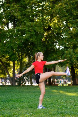 Genç sarışın bir kız parkta spor yapıyor, bir kadın da sokakta ısınıyor. Aktif açık hava eğitimi 