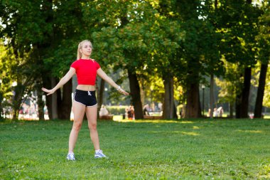 Genç sarışın bir kız parkta spor yapıyor, bir kadın da sokakta ısınıyor. Aktif açık hava eğitimi 