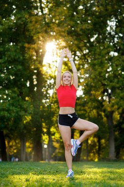 Bir bacağını dengede tutan beyaz bir kadın yoga savaşçısı, dışarıda, gün batımında sağlıklı bir kız, yaşam tarzı..