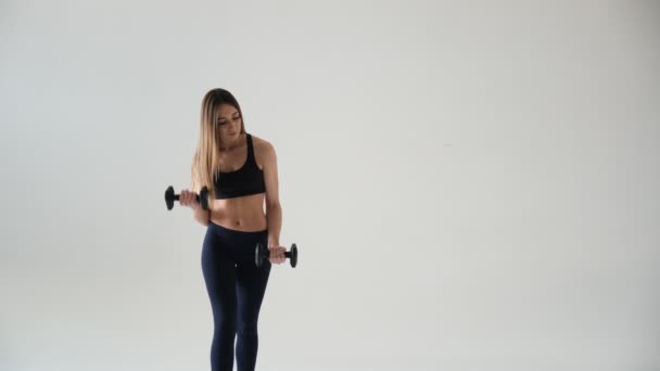 Schöne junge Frau macht Übungen mit Kurzhanteln am Bizeps. Foto athletische Frau mit perfektem Körper isoliert auf weiß — Stockvideo