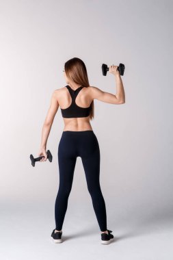 Güçlü kadın dambıllarla çalışıyor, kolunu esnetiyor. Beyaz arka planda spor giysili kadın fotoğrafı. Dikiz aynası. Tam uzunluk