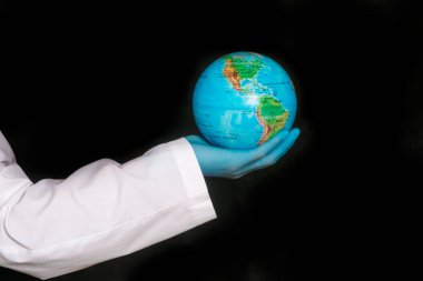 Dünya, siyah arka planda bir doktor önlüğü giymiş bir doktorun ellerinde. Viral salgın covid-19 konsepti. Coronavirüs salgını 2020.