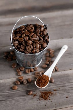 Küçük bir minyatür kovada Arap kahve çekirdekleri. Tahta arka planda beyaz seramik bir kaşıkta kahve.