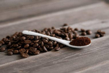  Tahta zemin üzerinde öğütülmüş kahve ile beyaz seramik kaşık. Kızarmış Arap taneleri..