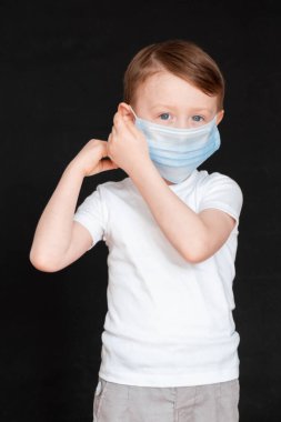 Küçük bir çocuk tıbbi maske tutuyor. Bebek yüz maskesi takıyor..