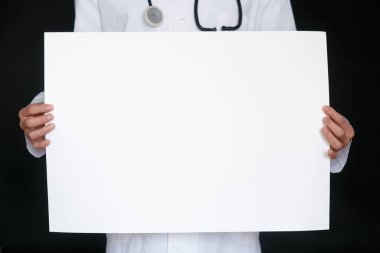 Siyah tişörtlü ve tıbbi eldivenli bir adam beyaz bir kağıt tutuyordu. Modelleme. Coronavirus. Karantinaya alın. Salgın hastalık. Uzayı kopyala Uyarı! Doktorun elinde mavi eldiven, elinde kağıtlar..