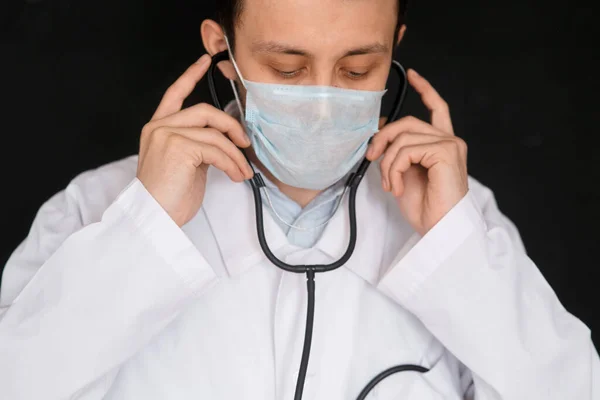 Male Doctor on a black background with a stethoscope in his hands close-up.