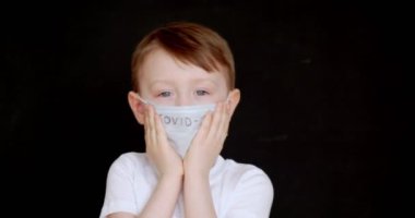 Maskeli bir çocuğun yakın çekimi var. Tıbbi maskeli bebek gülümsüyor..