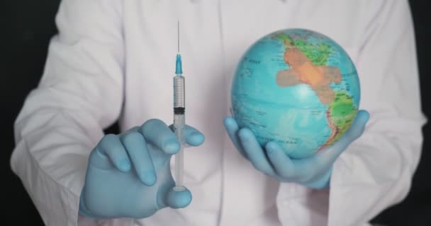 Земля світу в медичній масці і шприц в руках лікаря крупним планом на чорному тлі. Поняття — стокове відео