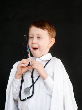 Doktor rolünde bir çocuk. Çocuk bir doktor mesleğini seçer. Siyah arka planda elinde şırınga var.