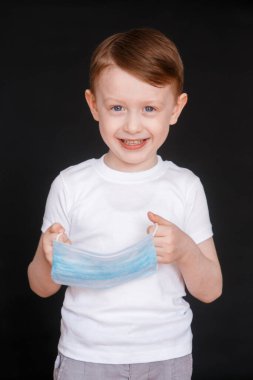 Küçük bir çocuk tıbbi maske tutuyor. Bebek yüz maskesi takıyor..