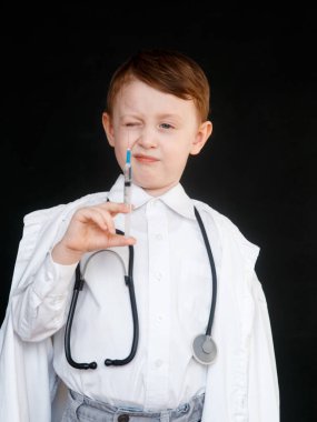 Doktor rolünde bir çocuk. Çocuk bir doktor mesleğini seçer. Siyah arka planda elinde şırınga var.