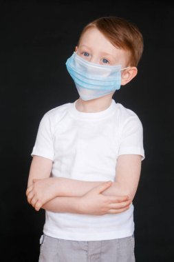 Küçük bir çocuk tıbbi maske tutuyor. Bebek yüz maskesi takıyor..