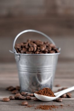 Küçük bir minyatür kovada Arap kahve çekirdekleri. Tahta arka planda beyaz seramik bir kaşıkta kahve..
