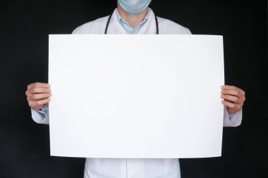 Siyah tişörtlü ve tıbbi eldivenli bir adam beyaz bir kağıt tutuyordu. Modelleme. Coronavirus. Karantinaya alın. Salgın hastalık. Uzayı kopyala Uyarı! Doktorun elinde mavi eldiven, elinde kağıtlar..