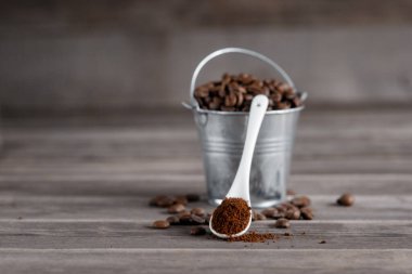 Küçük bir minyatür kovada Arap kahve çekirdekleri. Tahta arka planda beyaz seramik bir kaşıkta kahve.