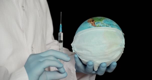 La terra di globo in una maschera medica e una siringa nelle mani del dottore primo piano su uno sfondo nero. Il concetto di — Video Stock