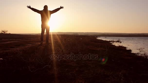 Silhouette of a man with hands raised in the sunset. Man with his arms wide open.