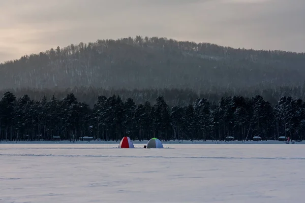 tents for winter fishing on a huge mountain lake. winter landscape. pure white snow. Fishermen catch fish in the fresh air. people\'s hobbies and sports
