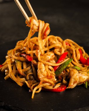 Ebi Udon. Soya soslu karides ve kızarmış sebzeli geleneksel Asya buğday eriştesi. Yukarıdan karanlık bir arkaplana doğru bak. siyah tahta tabaklar