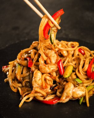 Ebi Udon. Soya soslu karides ve kızarmış sebzeli geleneksel Asya buğday eriştesi. Yukarıdan karanlık bir arkaplana doğru bak. siyah tahta tabaklar