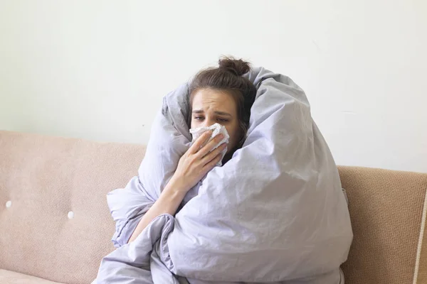 Chora młoda kobieta w kocu siedzi w domu z cieknącym nosem.. — Zdjęcie stockowe