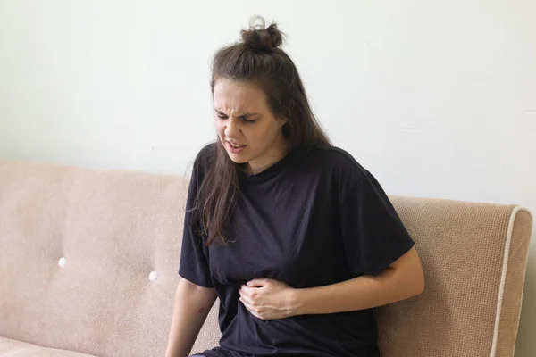 Молодая женщина страдает от боли в животе, сидя дома на диване — стоковое фото