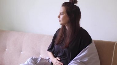 Karın ağrısı çeken genç bir kadın evinde, kanepede oturuyor.