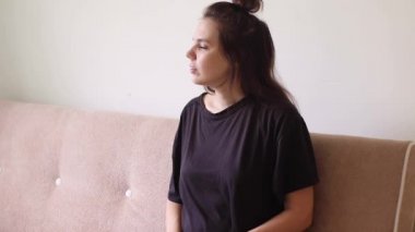 Karın ağrısı çeken genç bir kadın evinde, kanepede oturuyor.