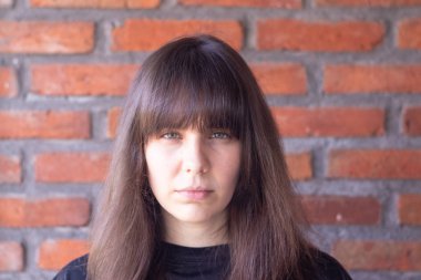 Portrait of a sad brunette woman with bangs wearing a black t-shirt on brick wall background