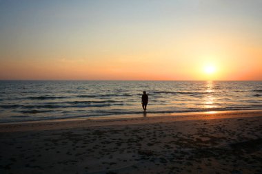 günbatımı ışığı altında sahilde yürüyen genç bir kadın