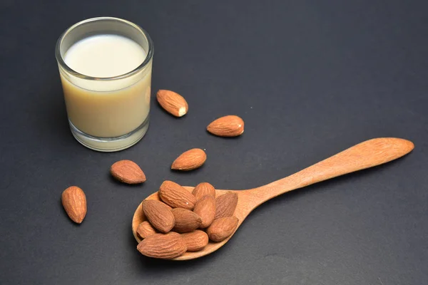 Миндальное молоко в стакане с миндалем в деревянной ложке — стоковое фото