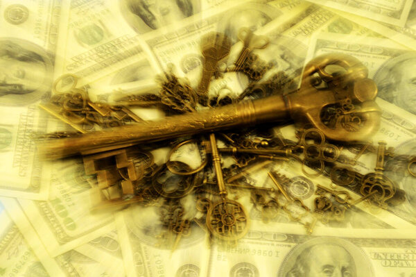 A lens blurred pile of brass keys with a larger dominant one centered on a background of American hundred dollar bills for creating a wealth strategy concept.