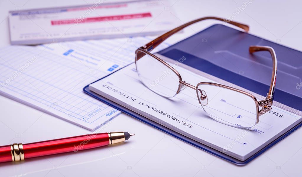 Pay with check instantly, on time. Glasses on a checkbook, red pen, financial documents on the background. Closeup, financial concept.