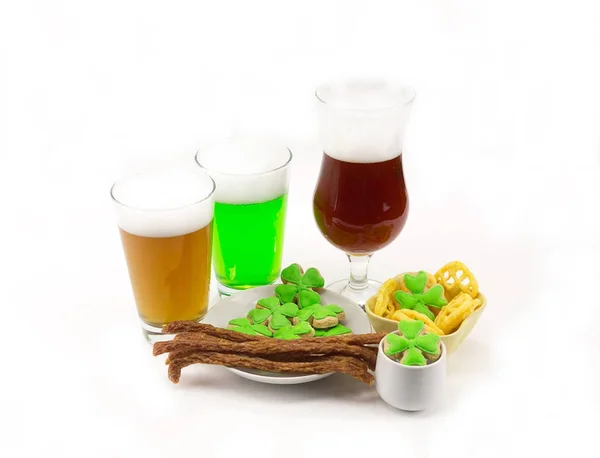 Light camp green and dark beer in a glass with appetizers on a table with clovers on a white background. The day of St. patrick