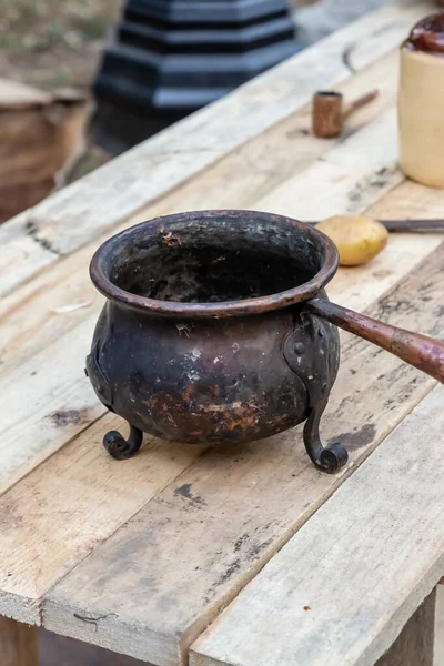 old mini bowler on a three-legged cast-iron pot stands on a wooden table, traditional kitchenware