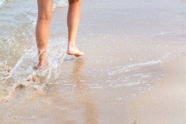 Okyanusun kumlu sahili boyunca yürü, kadın bacakları suda