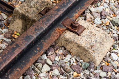 Eski paslı demiryolu çimento uykusuna sürgülenmiş. Arka planda çakılların olduğu kısma yakın plan.