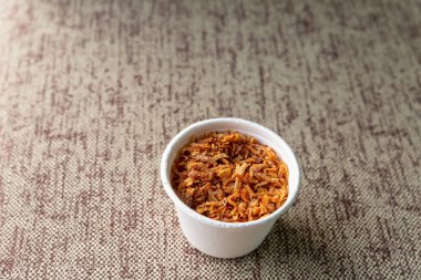 Kağıt bardakta katlanmış kuru ve karamelize soğanlar gri bir masada duruyor.