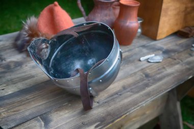 Vizörlü demir miğfer, baş aşağı, deri kayışlı tahta bir masada yatıyor.