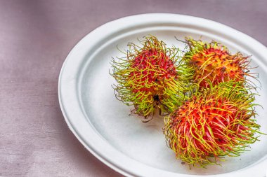 Rambutan pembe tüylü Asya meyvesi yakın plan bir tabakta yatıyor.