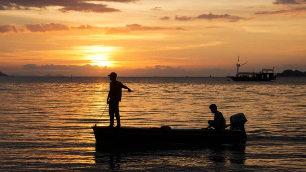 Silhouette of two fishermen on a small fishing boat with outboard motor on the ocean at nightfall. — Stock Photo, Image