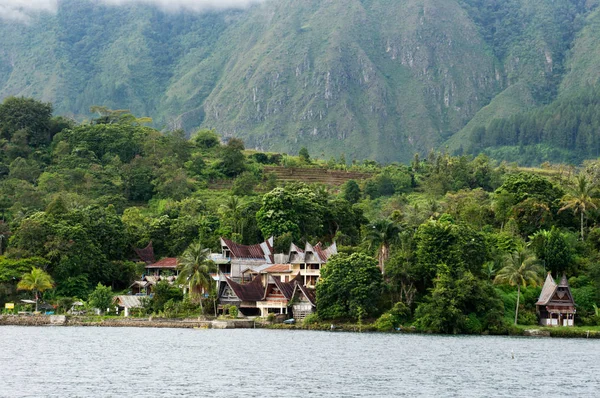 Mehrere Häuser am Fuße eines Berges neben einem See auf der Insel Sumatra Samosir. — Stockfoto
