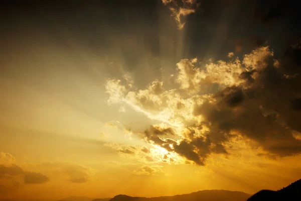 Sun setting behind the clouds and a silhouette of mountains at nightfal. — Stock Photo, Image