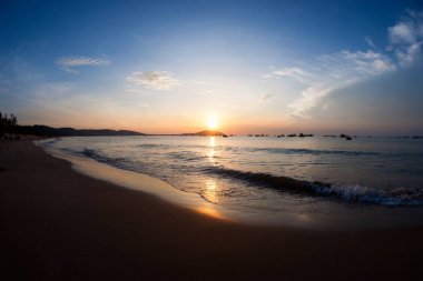 Altın renkli gündoğumu sırasında sabahları kumlu plajdan görülen denizde birkaç küçük balıkçı tekneleri silueti.