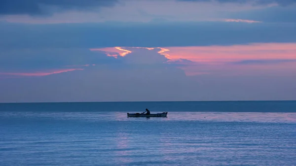 Fisherman silhouette in small fishing boat on the ocean at nightfall with orange sunset. — Stock Photo, Image