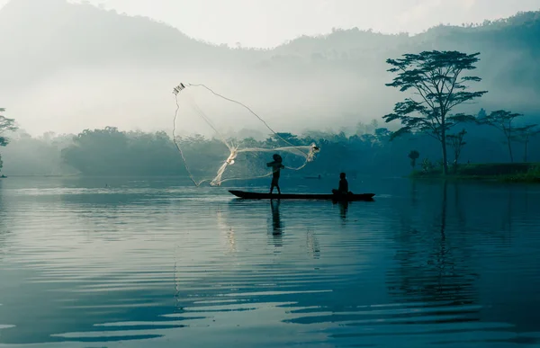 Fisherman casting out his fishing net in the river by throwing it high up into the air early in the morning.