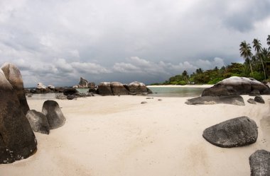Natural rock formation in sea and on white sand beach with palm trees in Belitung Island, Indonesia. clipart