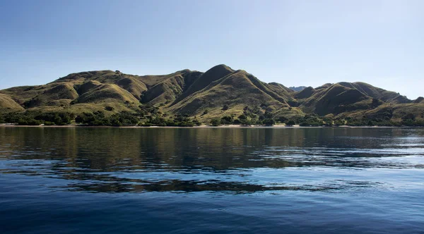 Ακτογραμμή των βουνών με πράσινη βλάστηση που αντανακλάται στο μπλε του ωκεανού νερό σε Labuan Bajo σε Flores. Royalty Free Φωτογραφίες Αρχείου